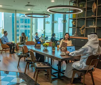 A dynamic shared workspace at Sahab Tower, Kuwait, where professionals collaborate and work individually in a bright, modern setting with large windows offering city views.