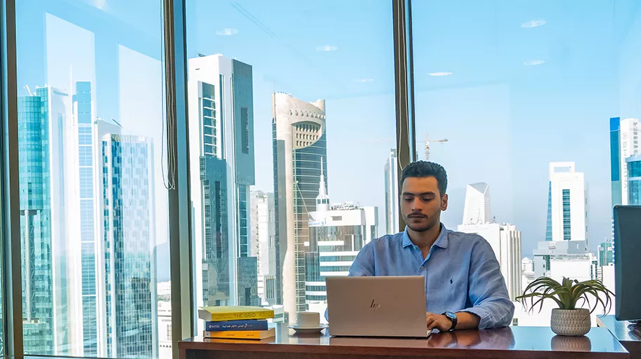 A professional working in a serviced office at Sahab Tower, Kuwait, with floor-to-ceiling windows offering stunning views of the city skyline.