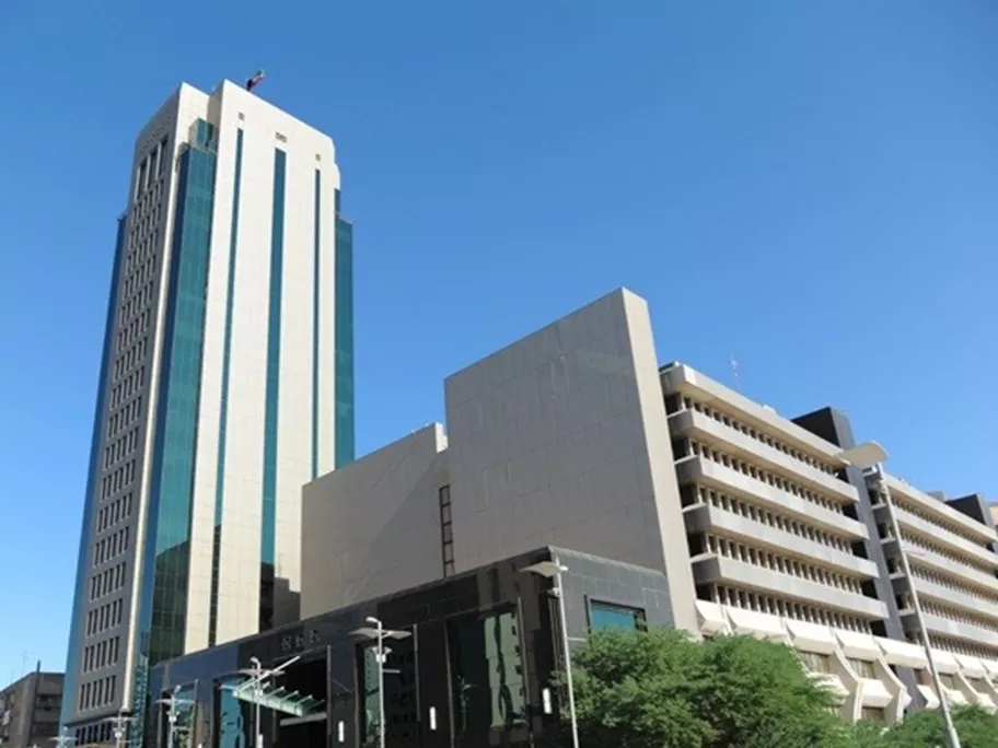 Sahab Tower in Kuwait, a tall, modern office building with a sleek glass façade, standing prominently against a clear blue sky alongside surrounding government and commercial buildings.